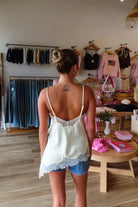 Cream, satin cami top with V neckline, asymmetric hem, scalloped lace trim, and adjustable straps, women’s lace going out top, date night lace top, asymmetrical hem top, girls night out top, vacation dinner outfit top