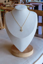 Gold necklace with a star pendant on a white bust against a neutral background
