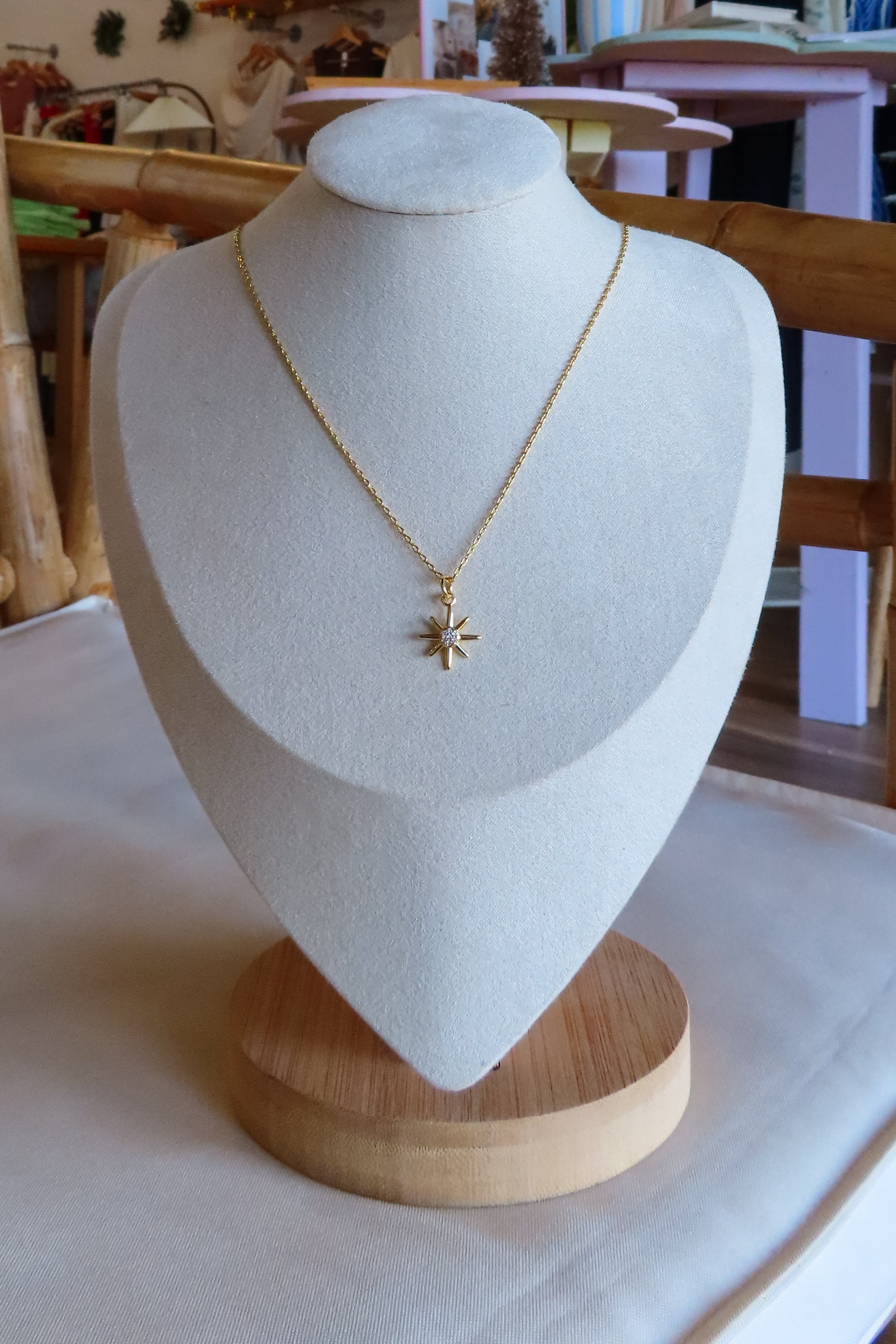 Gold necklace with a star pendant on a white bust against a neutral background