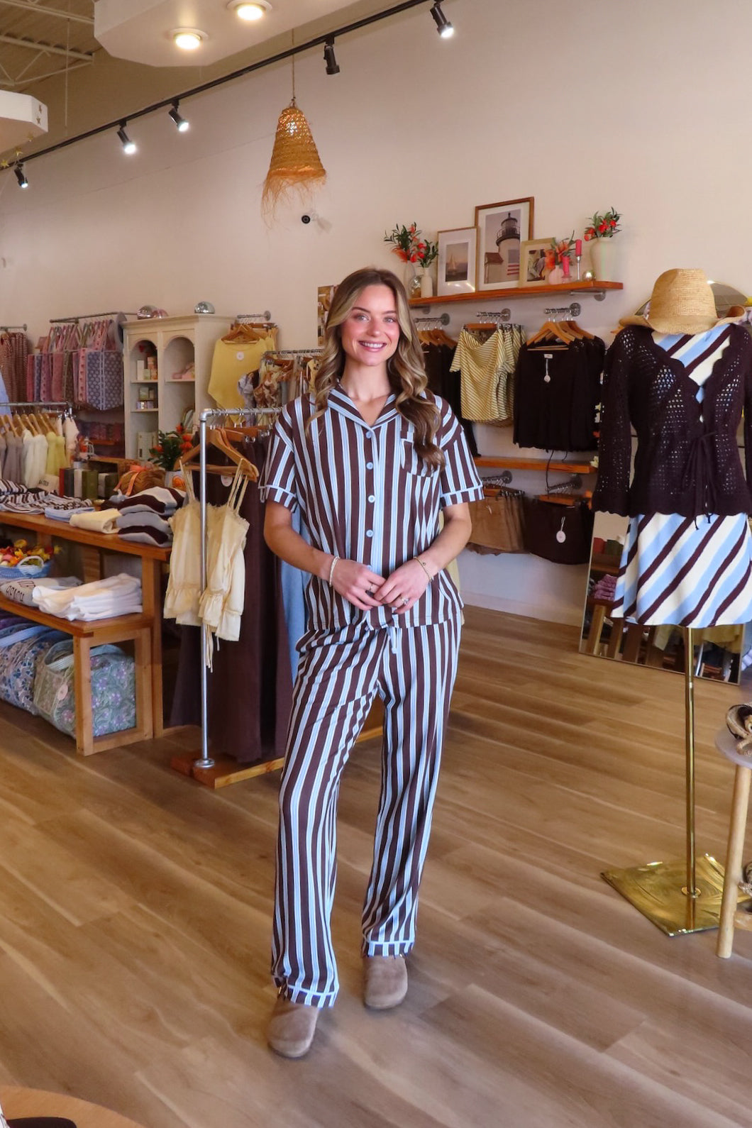 A woman modeling a matching short-sleeve button-up pajama shirt and striped pants set in a boutique clothing store.