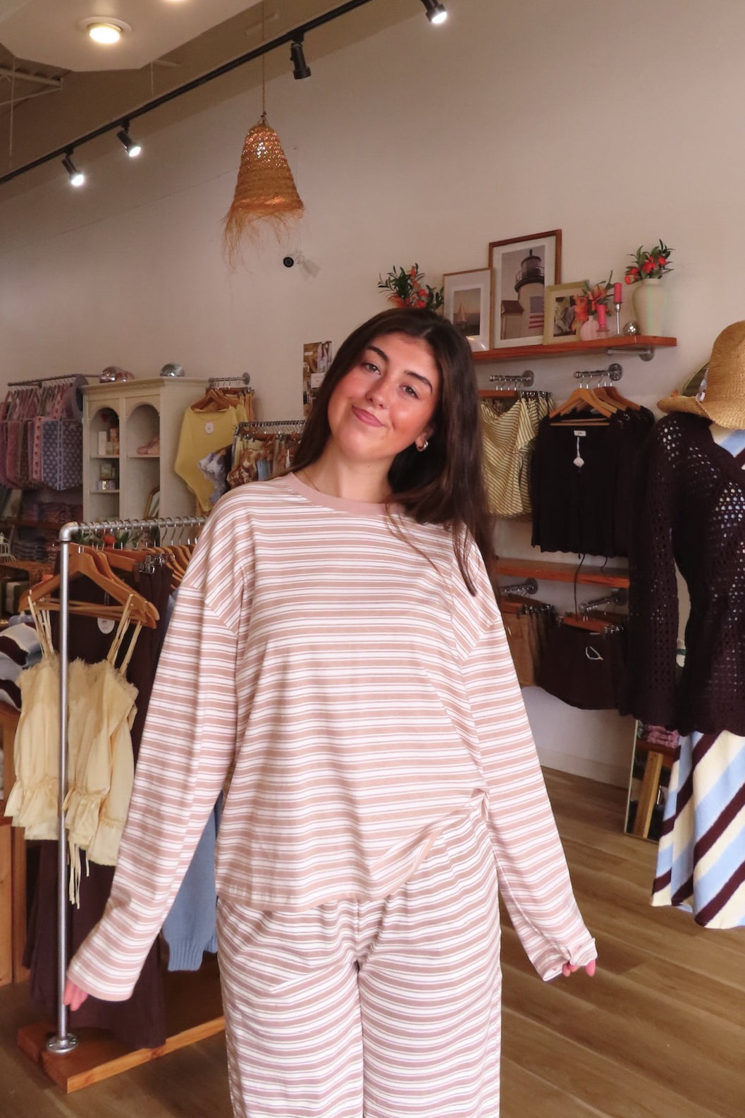 A woman modeling a matching two-piece lounge set with light pink and white horizontal stripes, standing inside a boutique clothing store.
