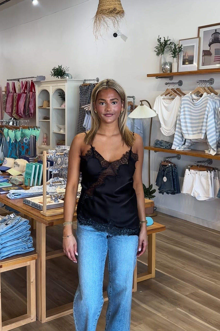 Black, satin cami top with V neckline, asymmetric hem, scalloped lace trim, and adjustable straps, women’s lace going out top, date night lace top, asymmetrical hem top, girls night out top, vacation dinner outfit top